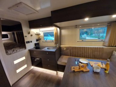 Intérieur moderne d'un camping-car avec cuisine, table et fenêtres lumineuses.