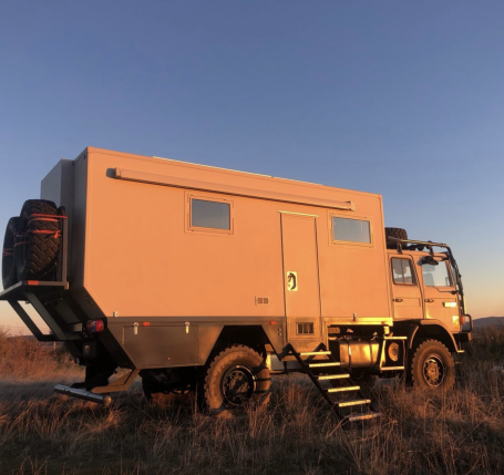 Camion aménagé beige avec des marches, en plein air au coucher du soleil.